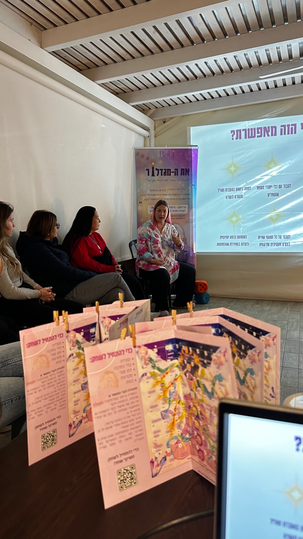 נס שמידט מרצה מול קהל נשים עם באנר לילא